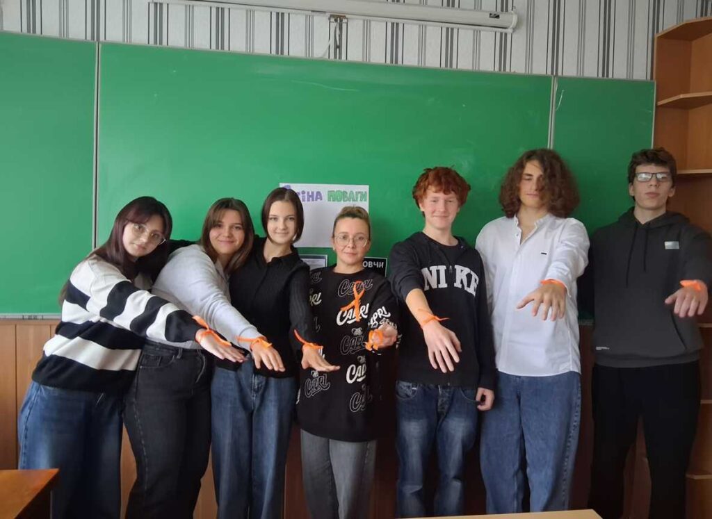 Група старшокласників та старшокласниць ліцею демонструють помаранчеві стрічки на зап'ястях біля класної дошки