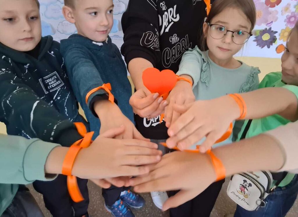 Учні молодших класів з помаранчевими стрічками на руках утворили коло єдності, тримаючи паперове серце під час акції 16 днів проти насильства