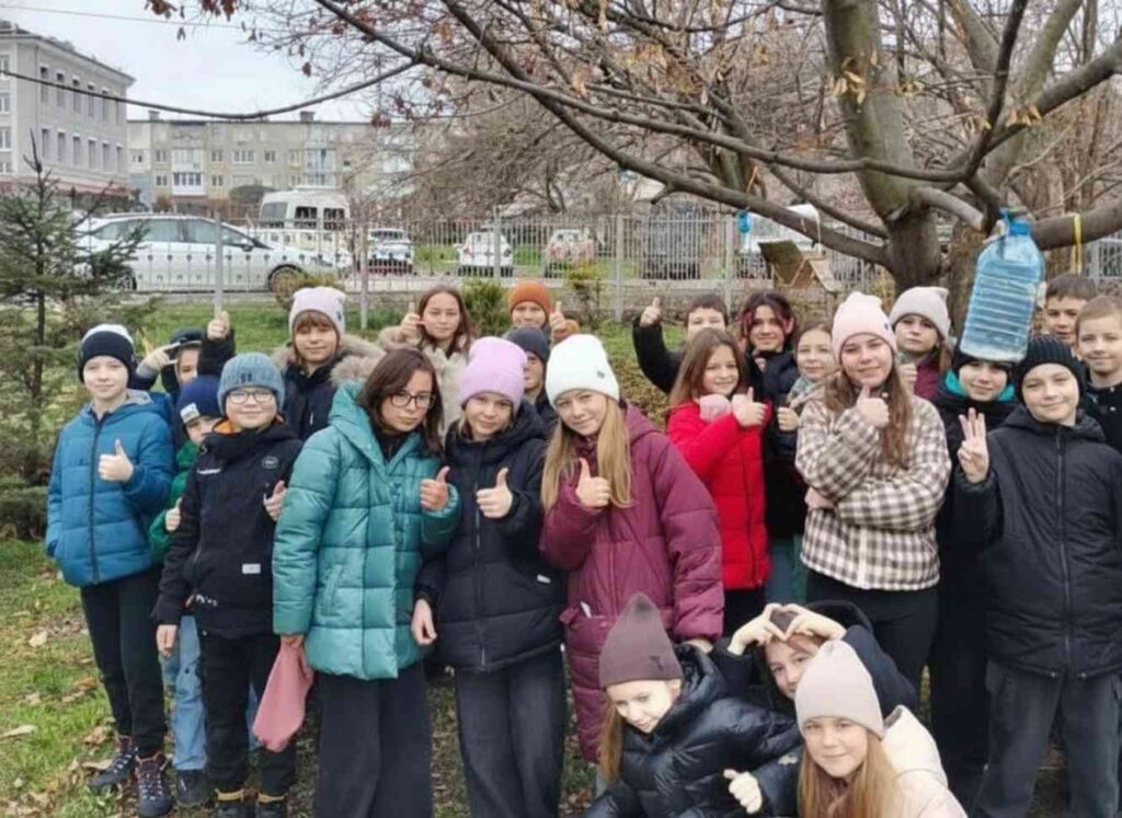 Велике спільне фото класу біля дерева з розвішаними годівничками