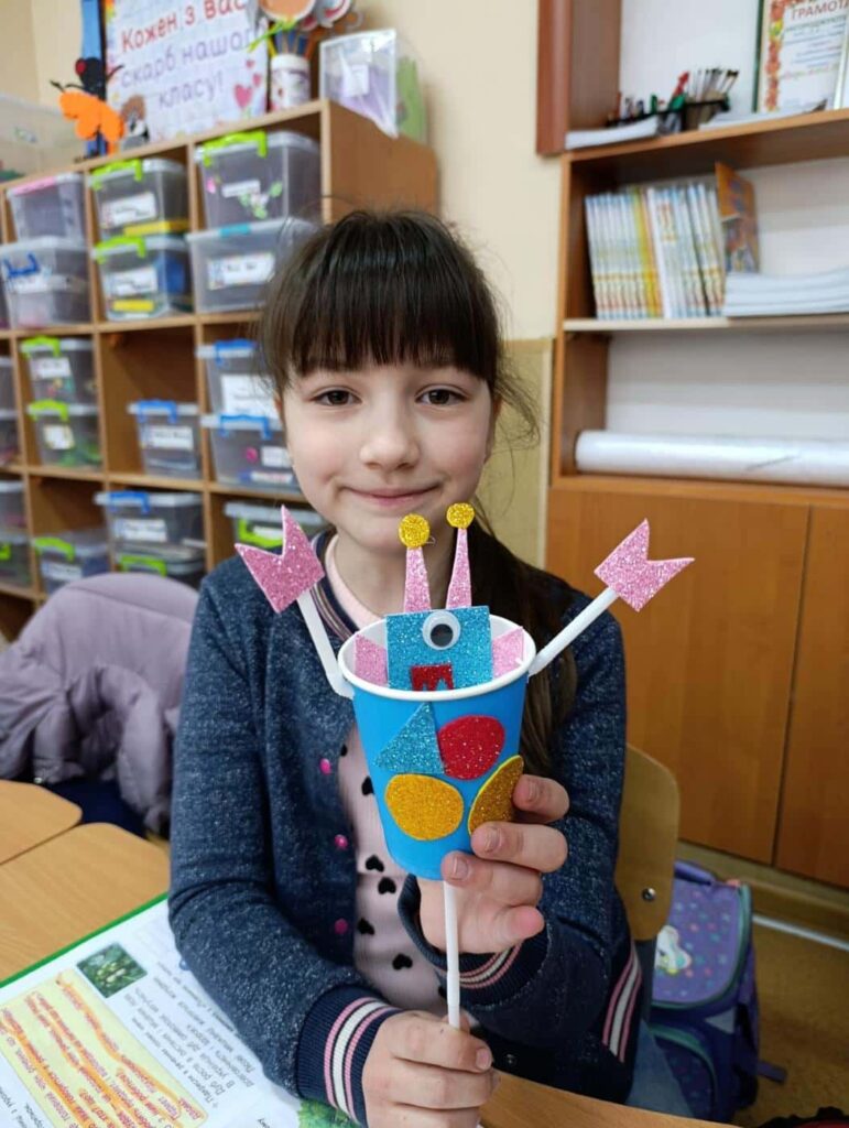 Дівчинка показує яскравого робота зі склянки, зробленого на Інженерному тижні у ліцеї